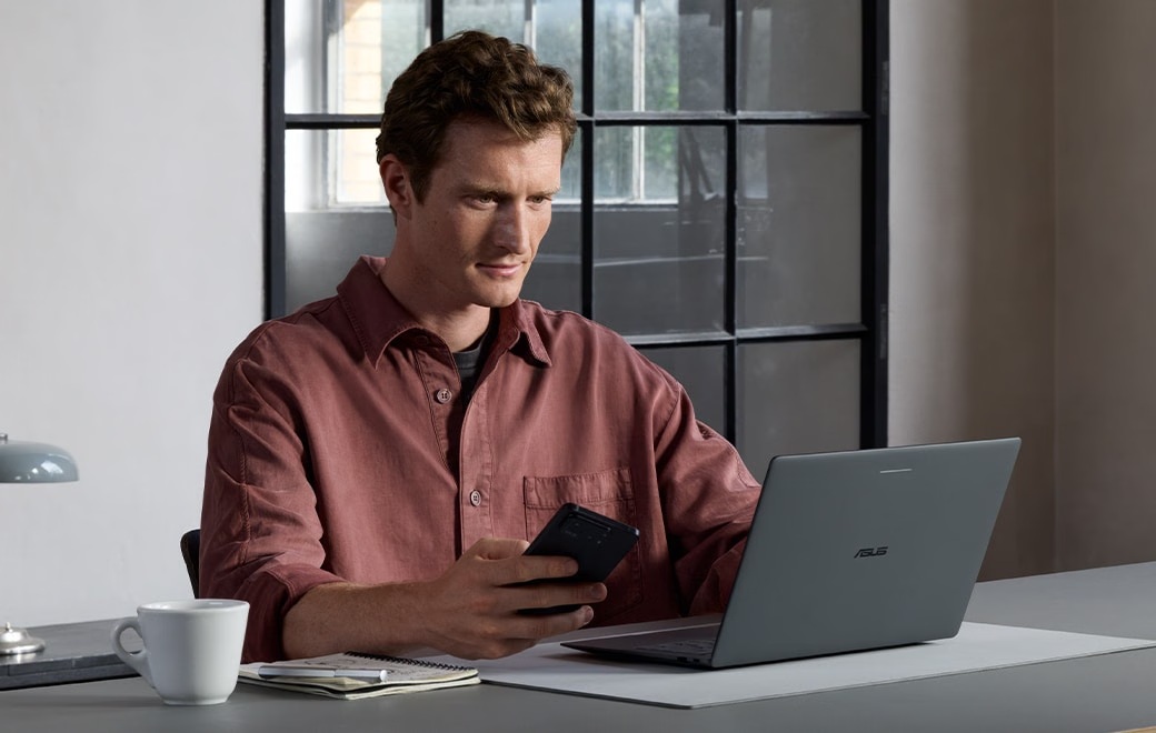 Man using an Android phone beside an ASUS Googlebook 14