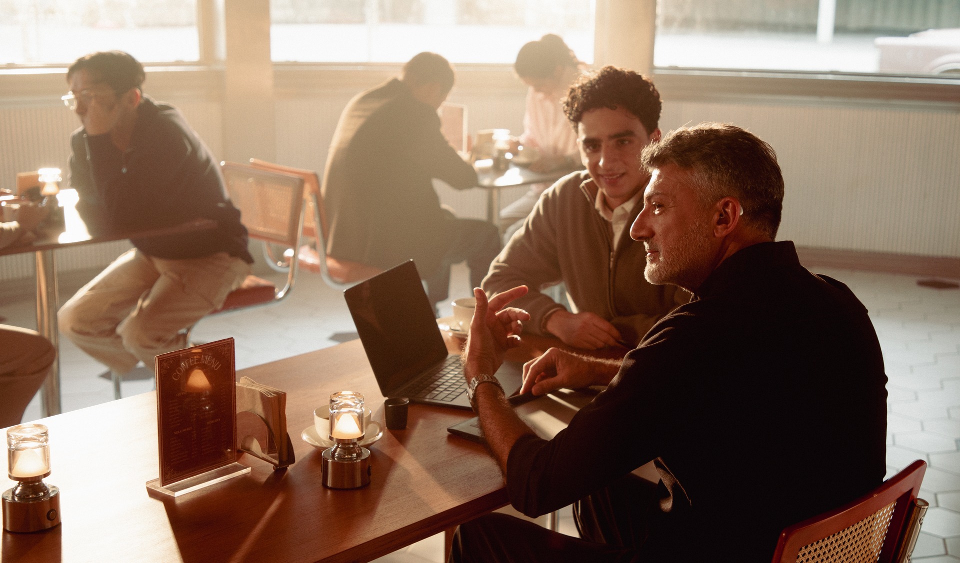 Two men talking at a cafe table in an ELEHEAR promotional lifestyle photograph.