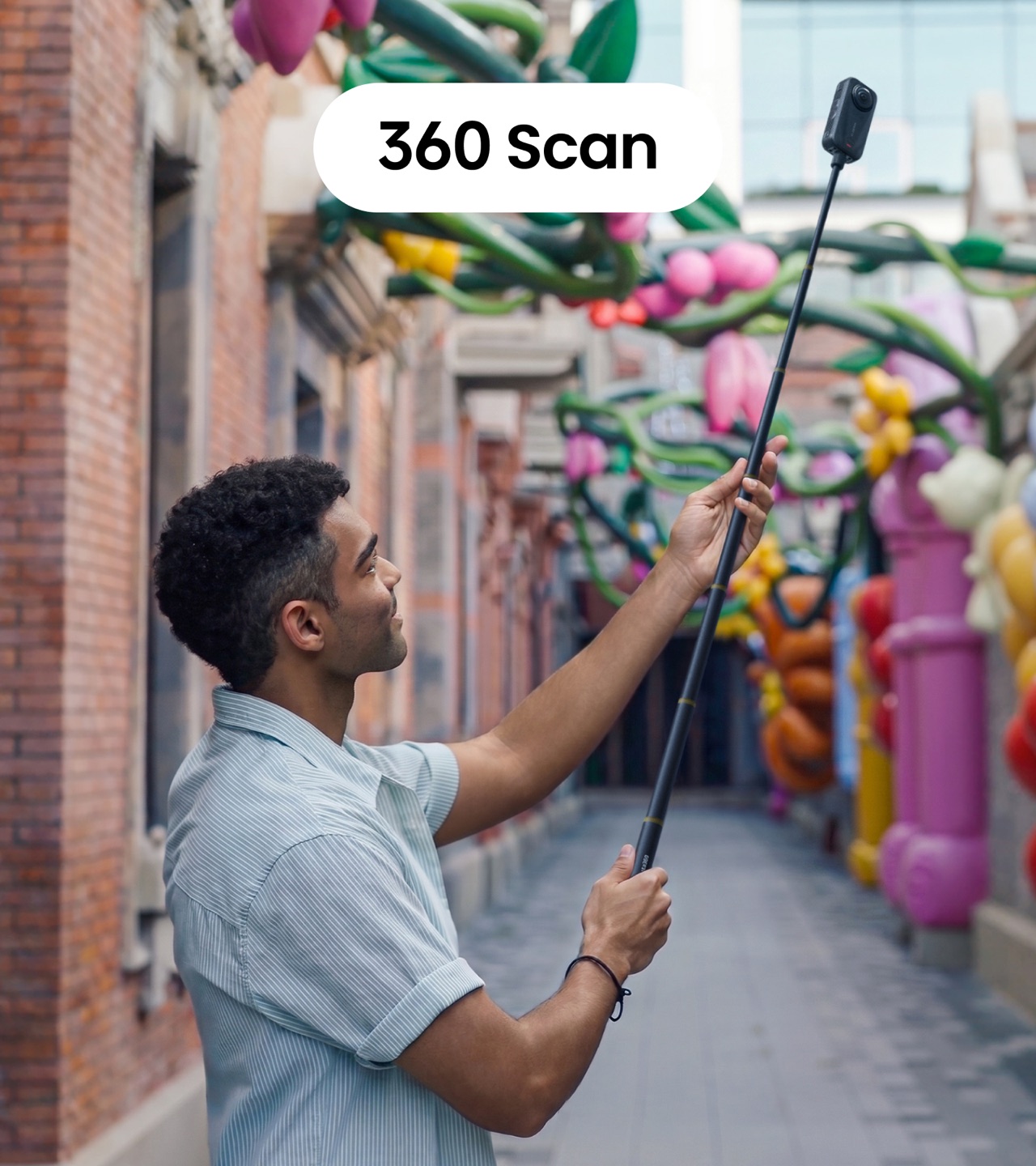 A person holds an Insta360 camera overhead on a selfie stick to scan a decorated passageway
