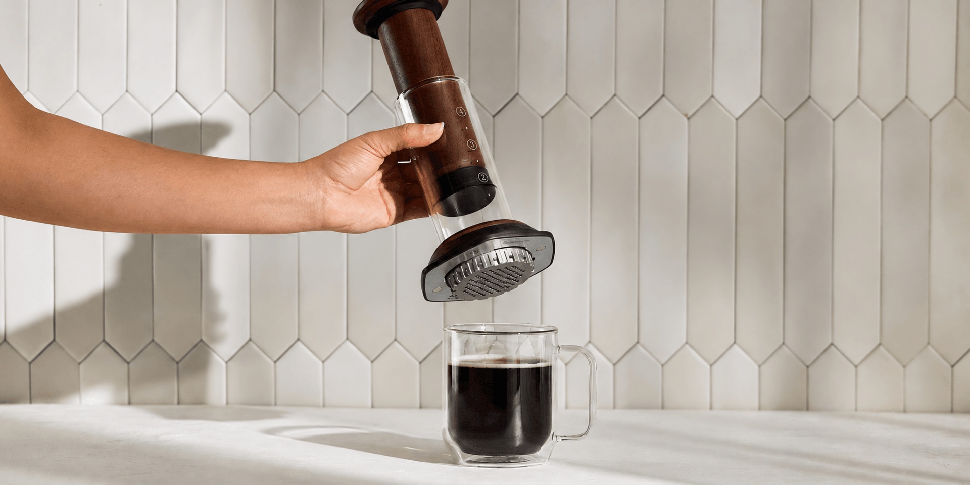 AeroPress Premium Walnut lifted above a mug after pressing coffee