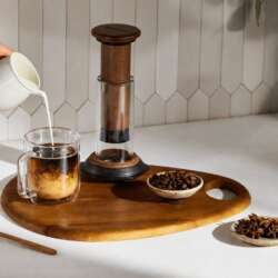 AeroPress Premium Walnut beside iced coffee and walnut brewing tools on a kitchen counter