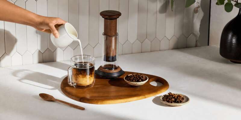 AeroPress Premium Walnut beside iced coffee and walnut brewing tools on a kitchen counter