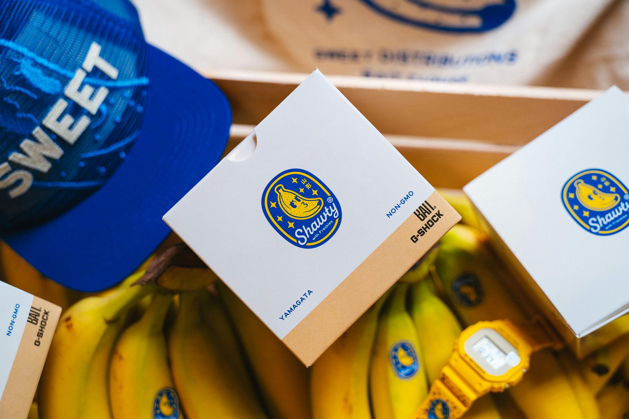 BAIT Yamagata's Finest watch boxes and blue cap arranged with bananas.