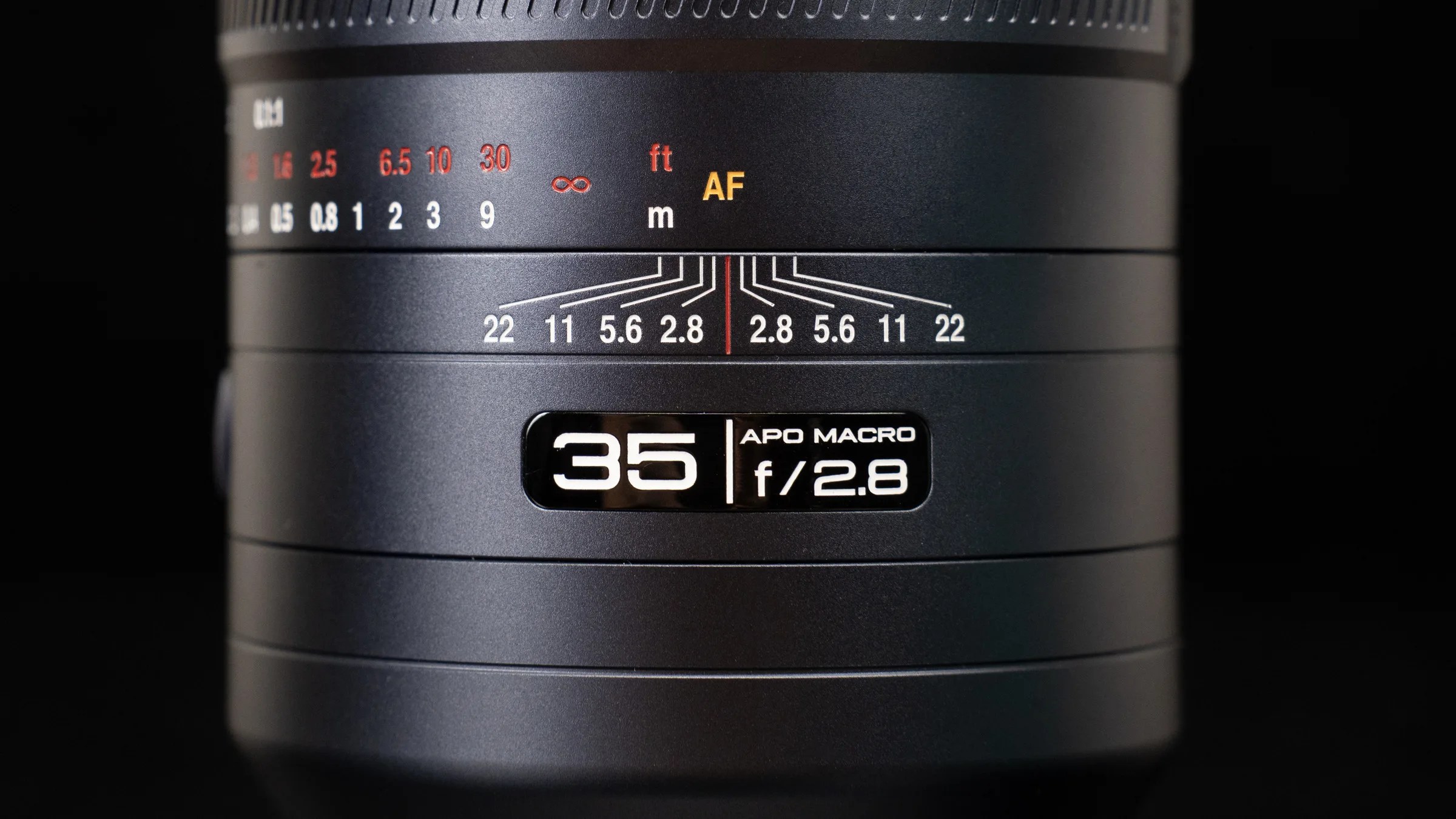Close-up of the Laowa 35mm f/2.8 APO Macro badge and engraved distance scales against black.