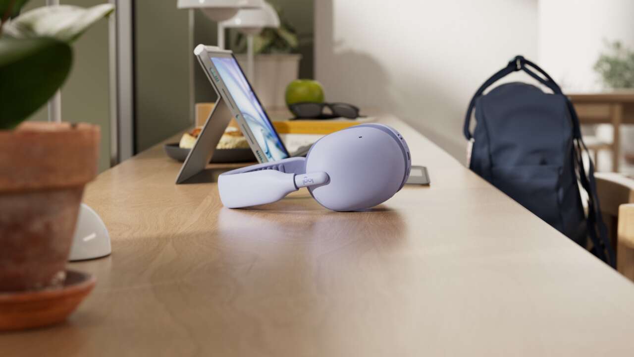 Lilac Logitech Zone Vibe Pro headphones on a cafe table beside a tablet and backpack.