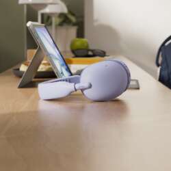 Lilac Logitech Zone Vibe Pro headphones on a cafe table beside a tablet and backpack.