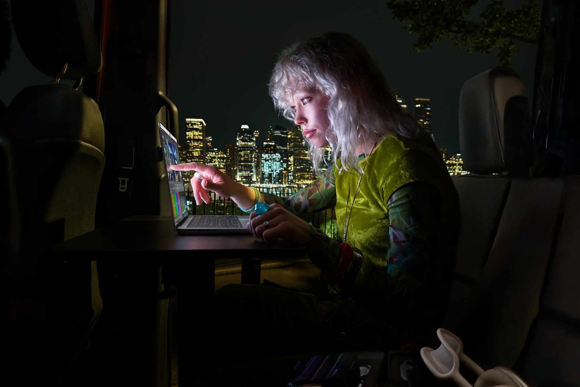 A user works on MacBook Pro with PROLED XDR Display in the dark with a bright cityscape behind them.