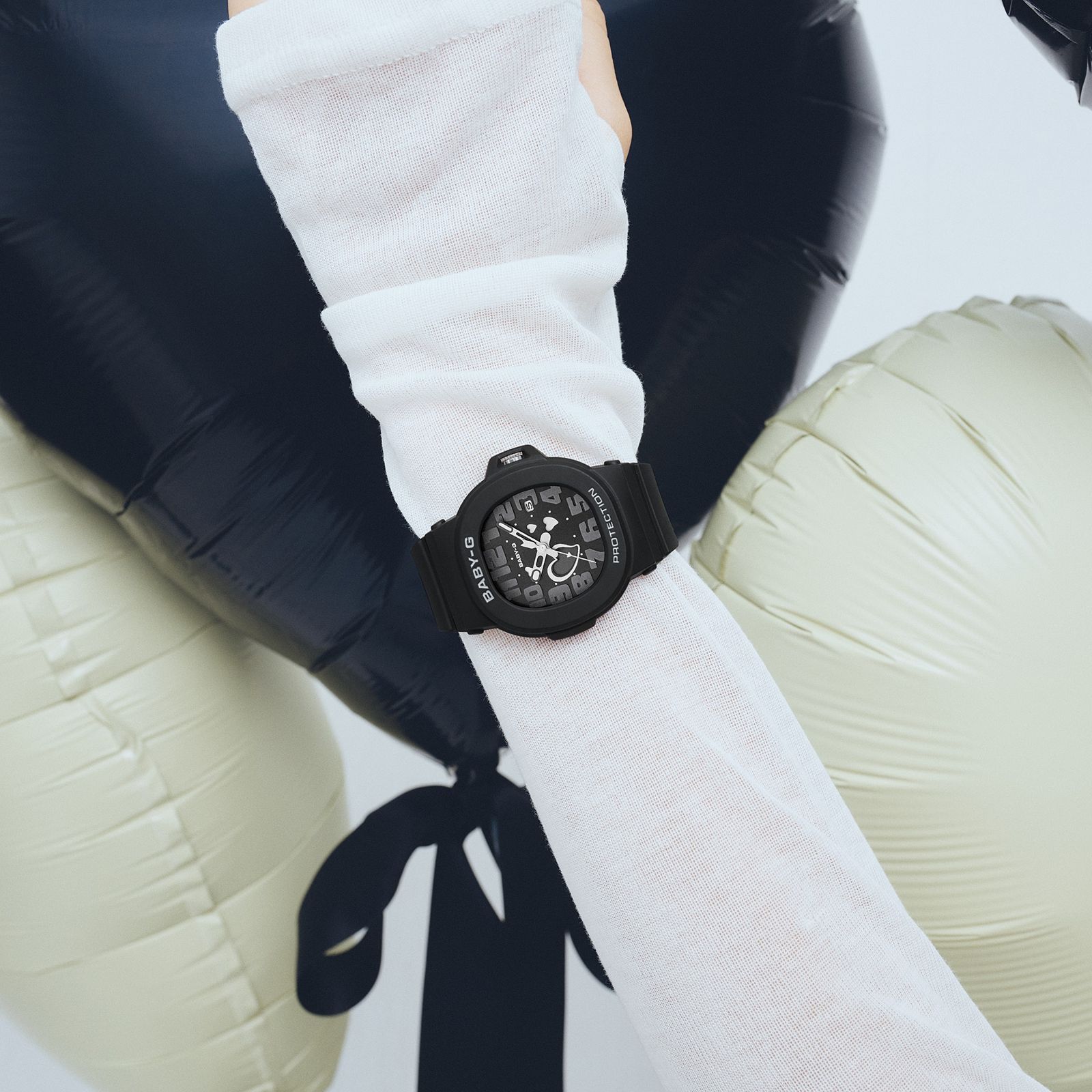 Black Casio BABY-G BGA-10 worn over a white sleeve beside heart balloons