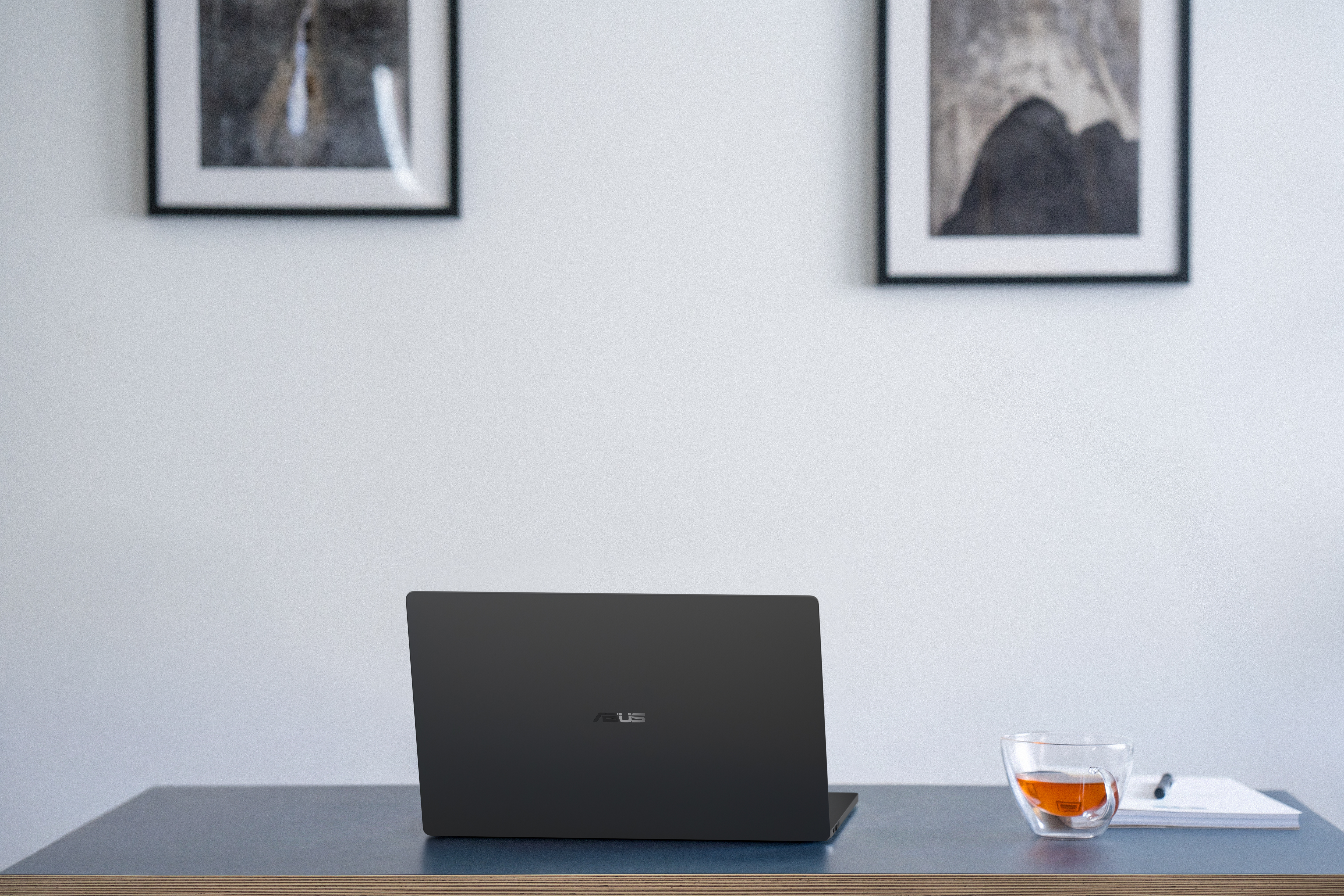 An open Eclipse Black ASUS ExpertBook A7 sits on a desk beside a cup, viewed from behind.