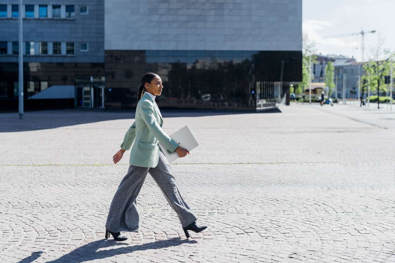 A woman carries a closed silver ASUS ExpertBook A7 through a city plaza.