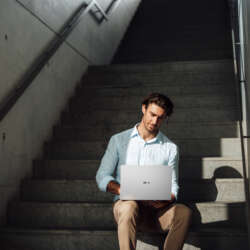 A man uses a silver ASUS ExpertBook A7 while sitting on concrete steps.