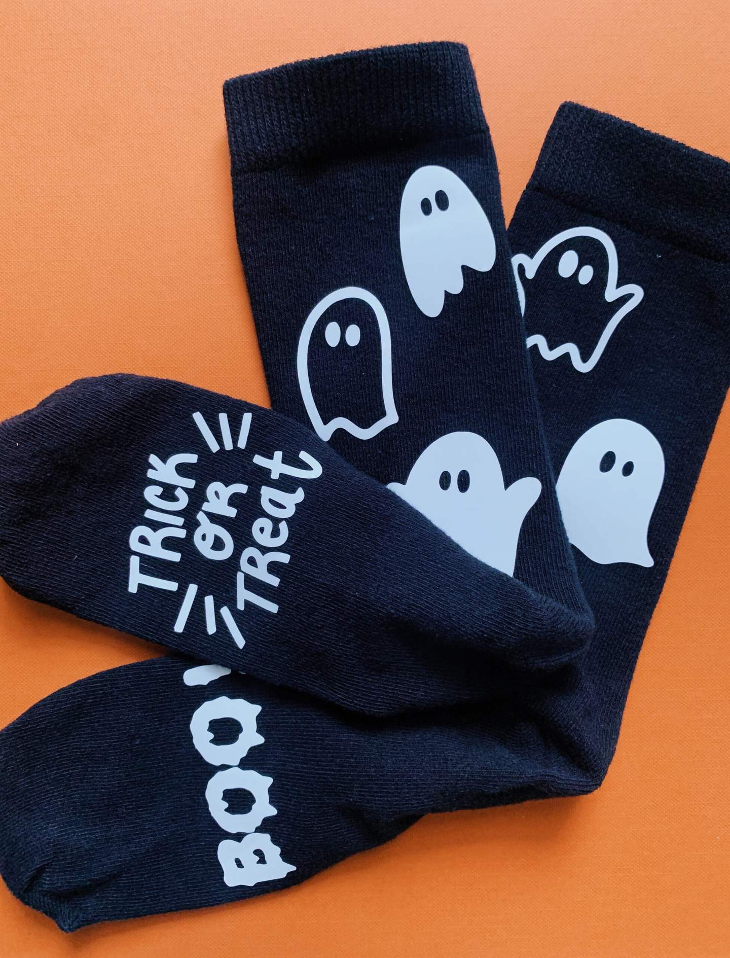 Black socks with ghost and Halloween lettering designs on an orange background