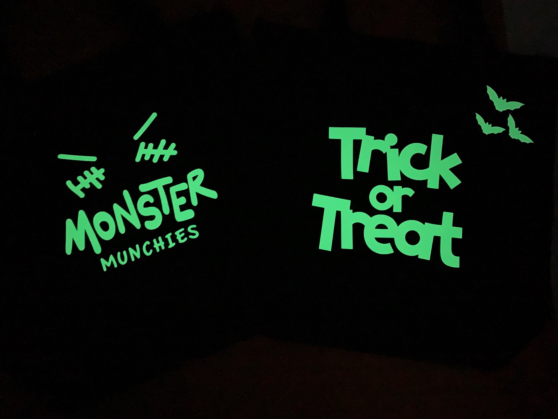 Two Cricut Halloween tote designs glowing green in a dark setting