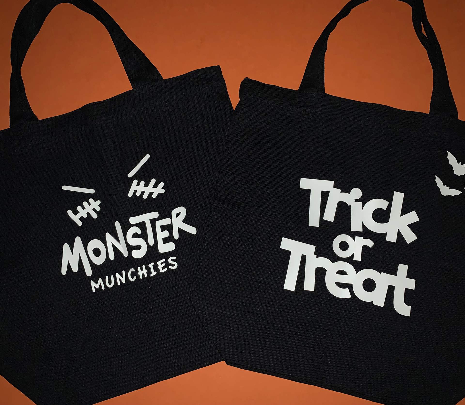 Two black Halloween candy totes with letters, a face and bats
