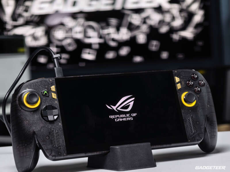 Black and gold ASUS ROG Xbox Ally X20 on a stand with its display powered on.
