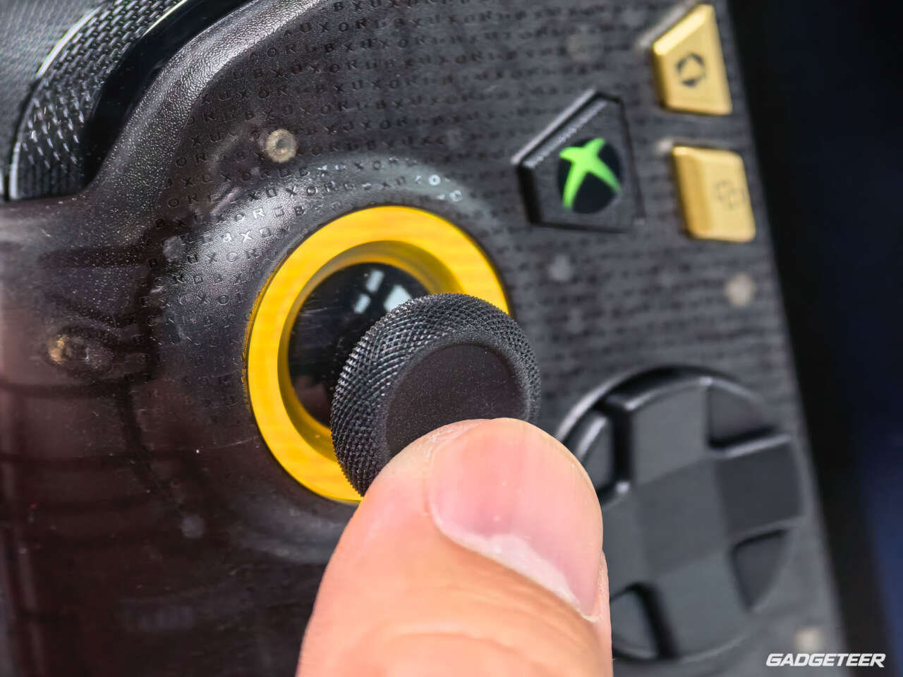 A thumb resting on the gold-ringed ROG Xbox Ally X20 thumbstick.