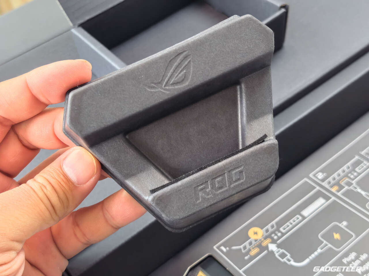 A folding ROG-branded stand held above the open handheld packaging.