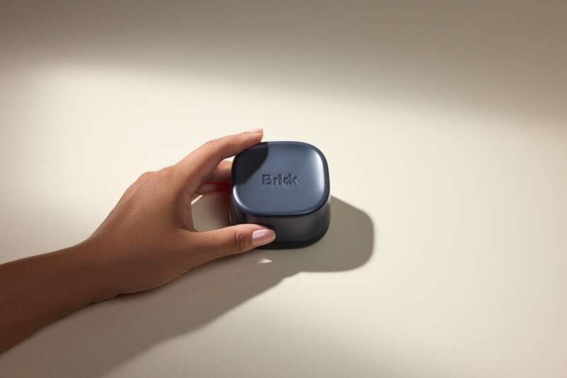 A hand holds the midnight-blue Brick Night device on a sunlit tabletop.