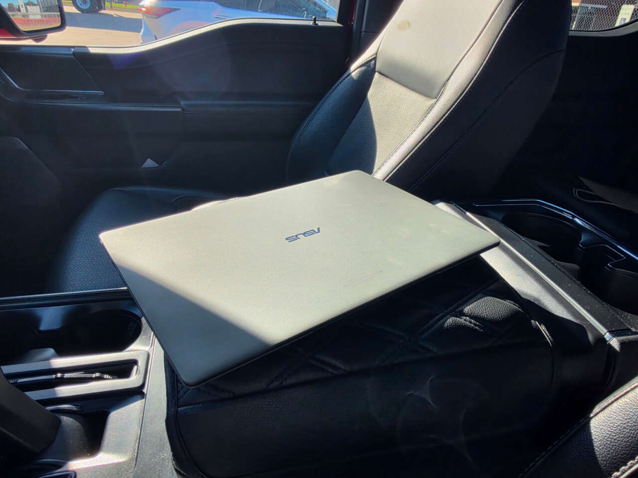 Closed ASUS Googlebook 14 on a dark vehicle seat.