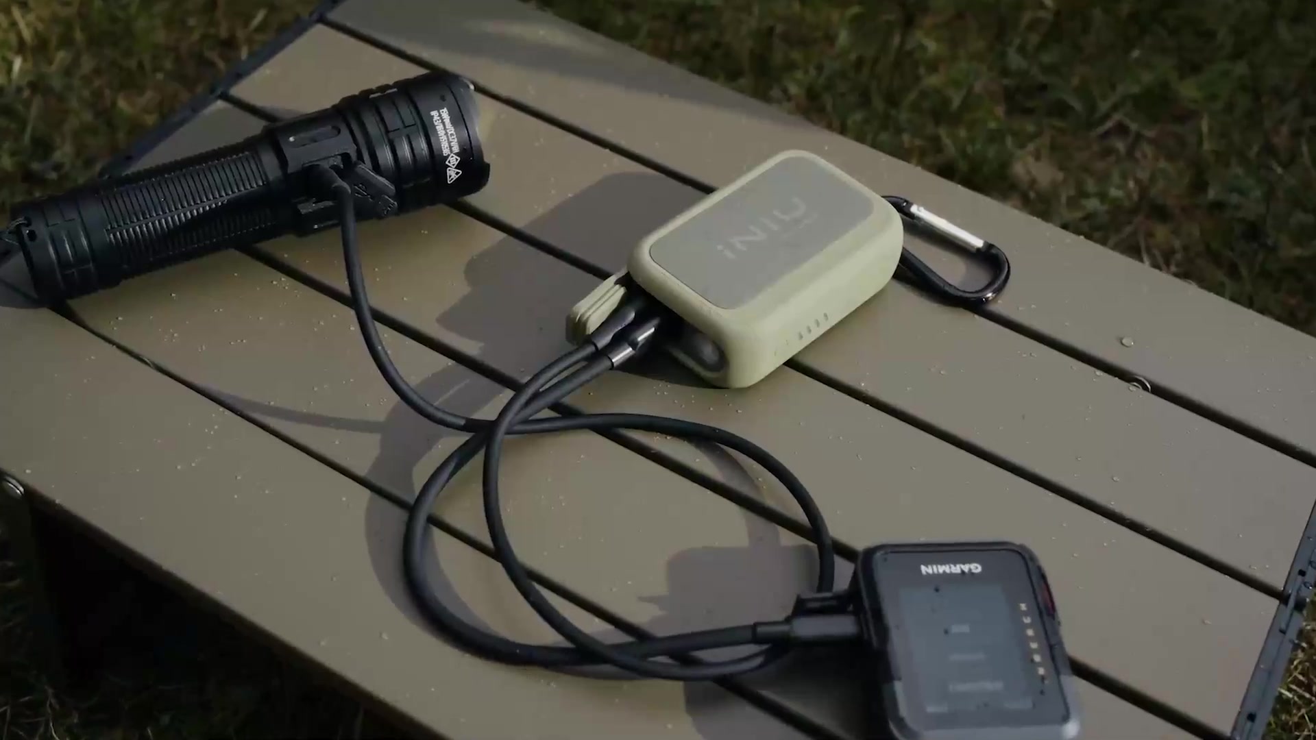 Ranger Green INIU Rugged 10000 connected by two USB-C cables to devices on a camping table.