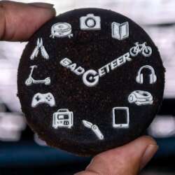 A used espresso coffee puck held between fingers, with The Gadgeteer logo and icons printed in white using the xTool O1 Omni.