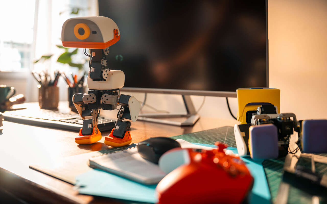 A cream Microduck standing on a desk beside a game controller