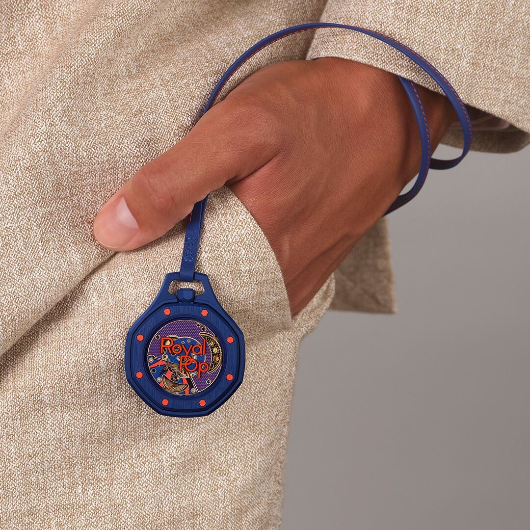 Royal Pop watch hanging from its blue and orange lanyard beside a trouser pocket