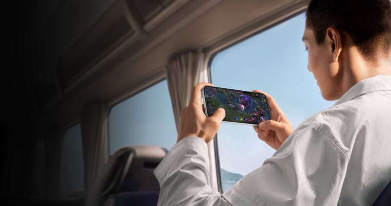 Person playing a game on an OPPO Find X10 Pro Max beside a train window.