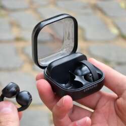 Hands holding black Samsung Galaxy Buds On and their open case outdoors