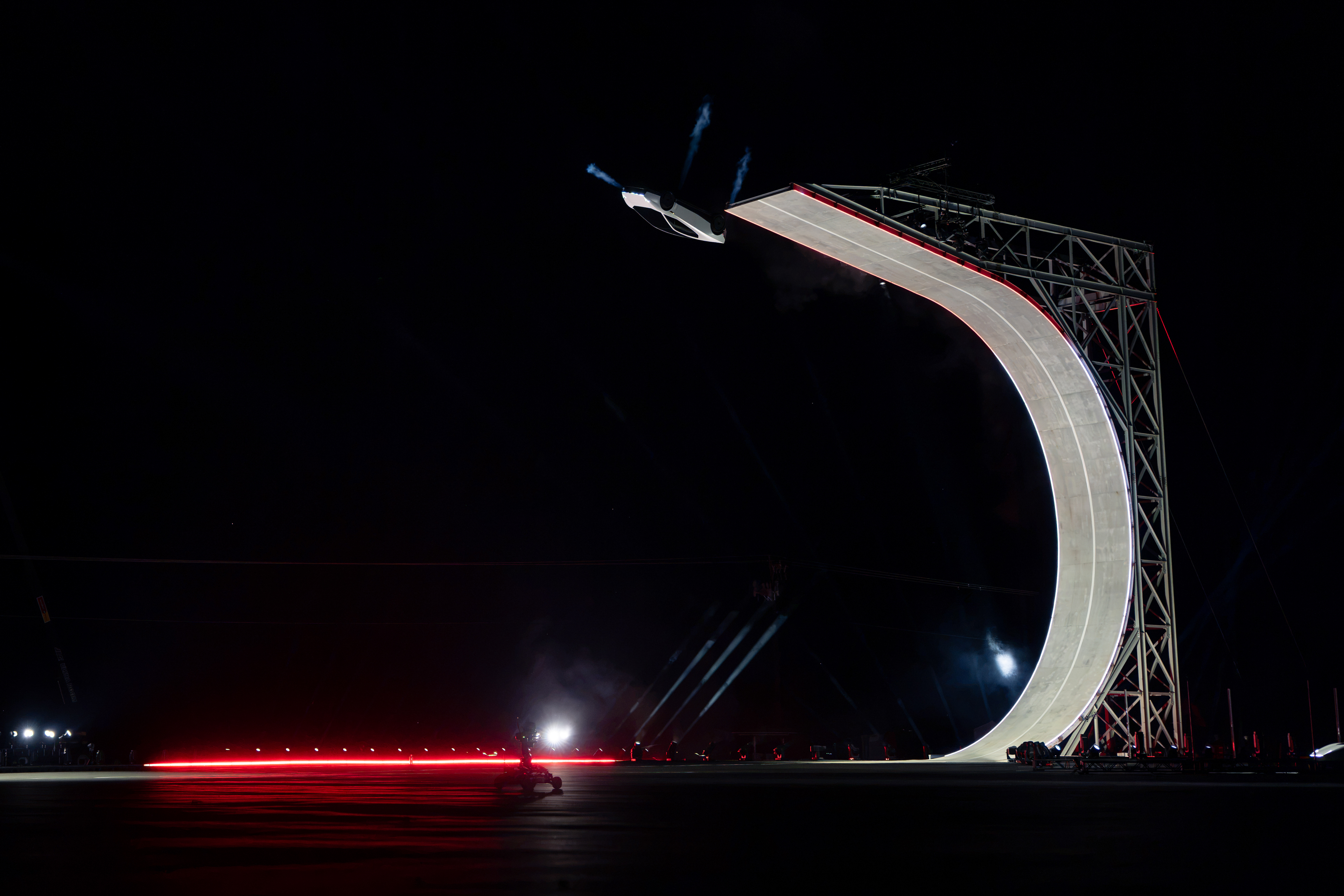 White Tesla Roadster inverted beside the upper edge of a curved ramp at night