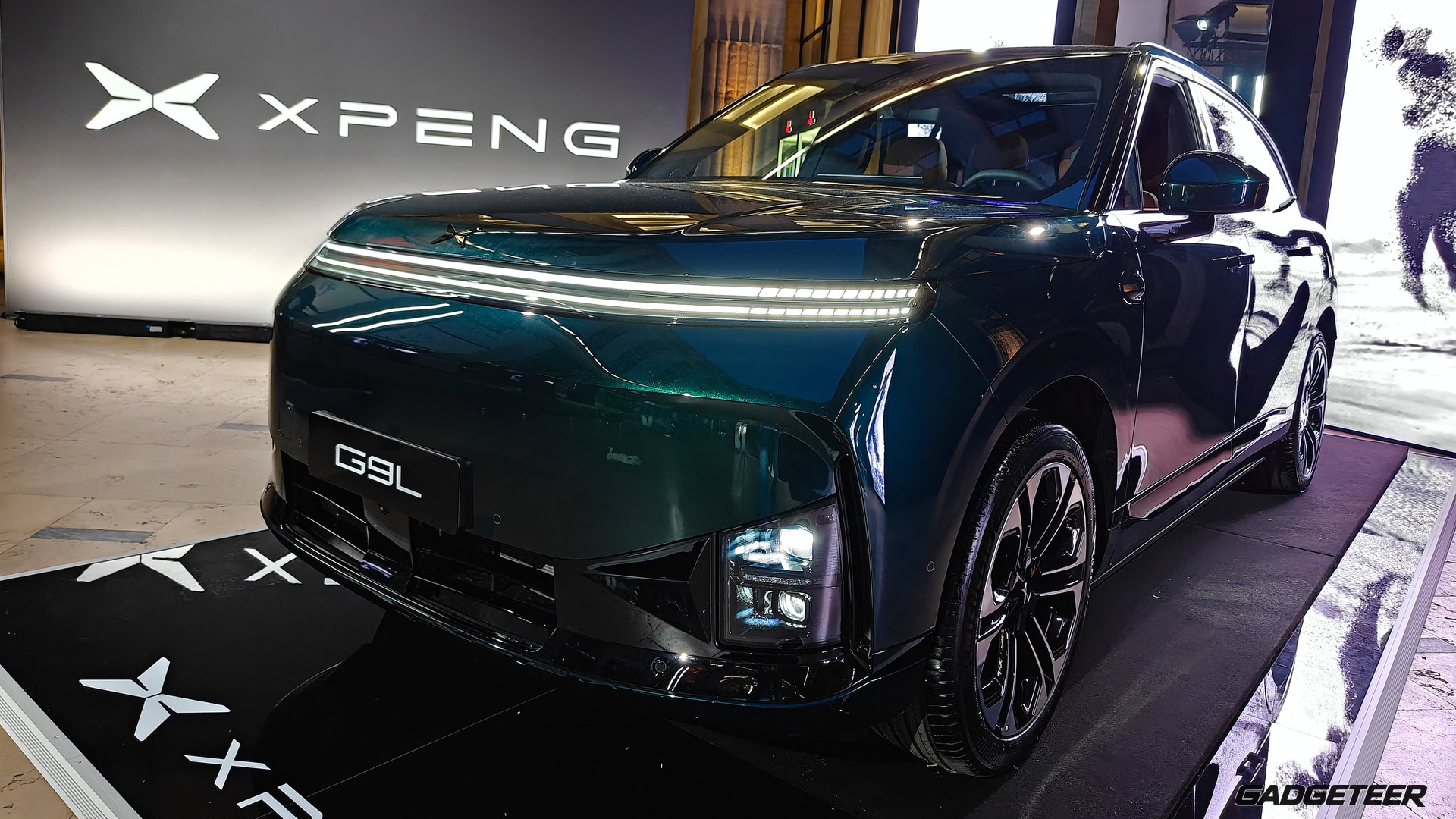 Green XPENG G9L viewed from the front three-quarter at the Paris event, with its G9L plate and XPENG display behind it.